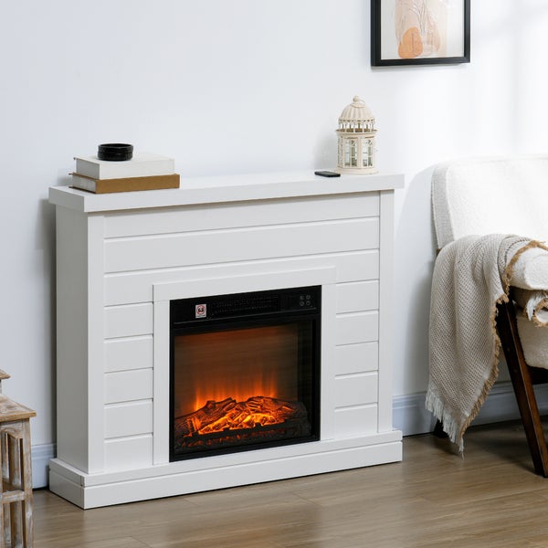 Weißer Elektrokamin mit Kaminumbau in Holzplanken-Optik, Flammeneffekt mit glühenden Holzscheiten, in einem hellen Wohnzimmer neben einem Sessel.