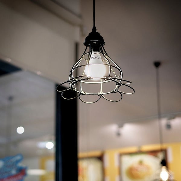 Industrielle Pendelleuchte mit schwarzem Drahtkäfig und brennender Glühbirne in einem hellen Raum.
