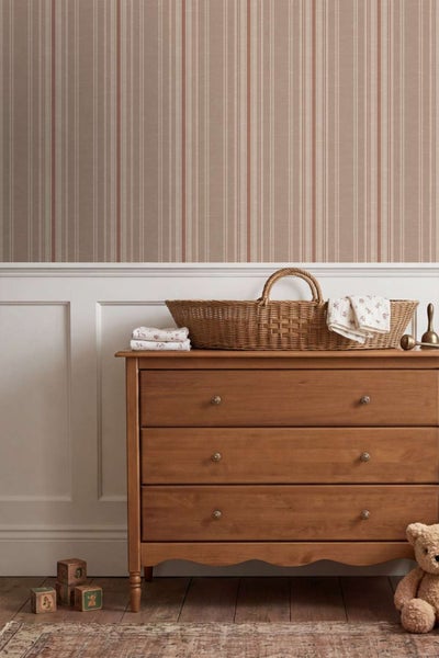 Vliestapete mit Längsstreifenmuster in einem Kinderzimmer mit Holzkommode und geflochtenem Weidenkorb vor weißer Wandverkleidung