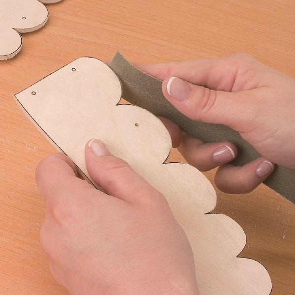 Person schleift eine Holzzuschnitt Form mit Schleifpapier glatt.