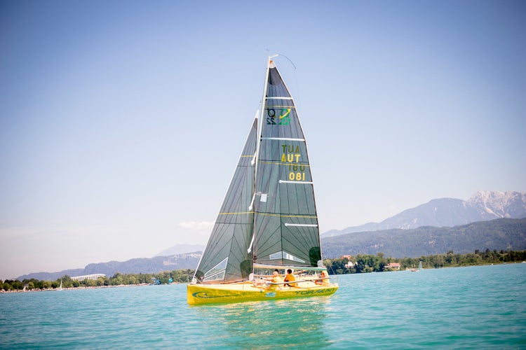 Ein Segelboot auf einem See vor einer Bergkulisse bei sonnigem Wetter.