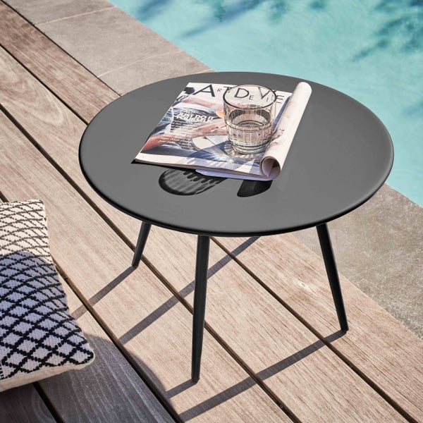 Runder schwarzer Beistelltisch aus Metall auf einer Holzterrasse am Pool mit einer Zeitschrift und einem Glas Wasser.