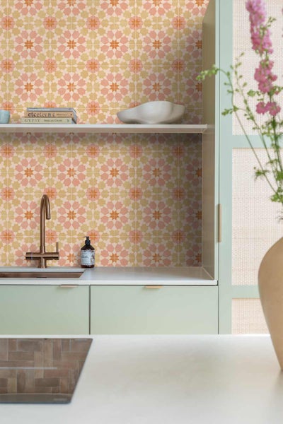 Küchenrückwand mit geometrischem Muster, Spüle mit goldfarbener Armatur und hellgrünen Küchenschränken im modernen Stil.