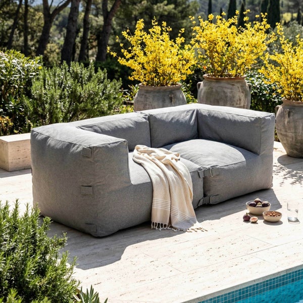 Modernes graues Outdoor-Loungesofa auf einer Terrasse am Pool, bestehend aus zwei Modulen mit einer Decke und Gartenpflanzen.