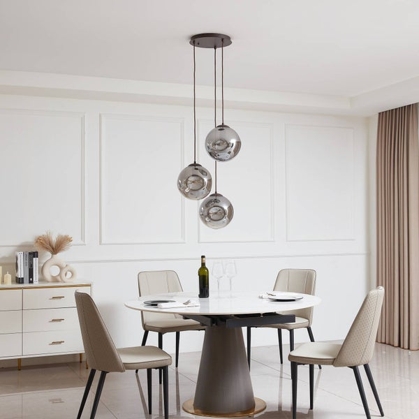 Modernes Esszimmer mit dreiflammiger Pendelleuchte mit kugelförmigen Glasschirmen über rundem Esstisch mit vier beigen Stühlen.