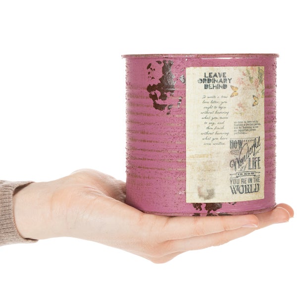 Kleiner zylindrischer Metallbehälter in Rosa mit dekorativem Etikett im Vintage-Stil, präsentiert auf einer Handfläche.