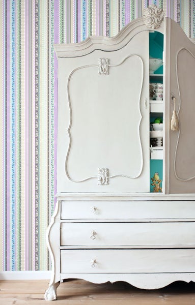 Antiker weißer Schrank mit Schubladen vor gestreifter Tapete