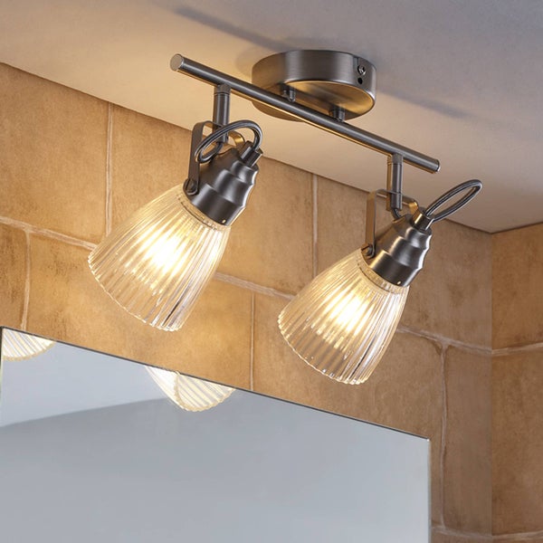 Zweiflammiger Deckenstrahler aus gebürstetem Metall mit geriffelten Glasschirmen, montiert im Badezimmer über einem Spiegel.