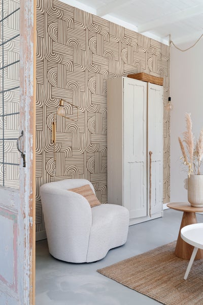 Wohnzimmer mit geometrischer Tapete, Sessel und Holzmöbeln für ein gemütliches Ambiente.