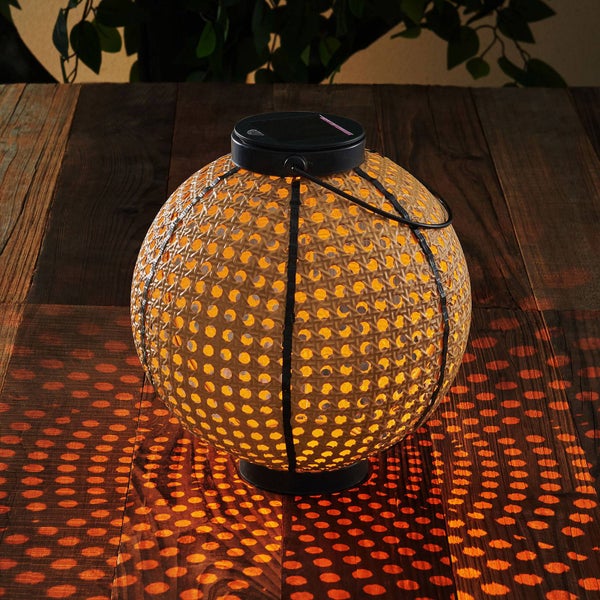 Runde Solarleuchte in Korbgeflecht-Optik mit warmweißem Licht auf einer Holzoberfläche.