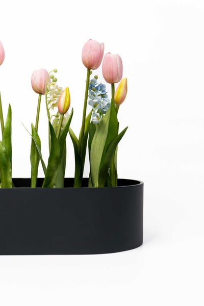 Schwarzer ovaler Pflanzkübel mit künstlichen Tulpen und Frühlingsblumen.