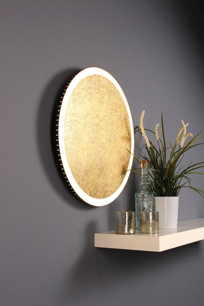 Moderne runde LED-Wandleuchte mit goldener Struktur-Oberfläche und Lichtring, montiert über einem Regal mit Pflanze und Glasaccessoires.