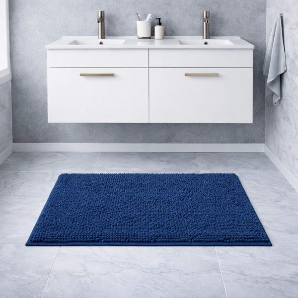 Rechteckige dunkelblaue Chenille-Badematte vor einem weißen Doppelwaschtisch in einem modernen Badezimmer mit grauen Fliesen.