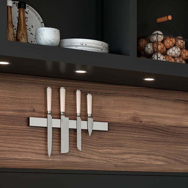 Magnetleiste für Messer an einer Küchenrückwand in Holzoptik unter einem Regal mit integrierten Spotlights und Küchenutensilien.