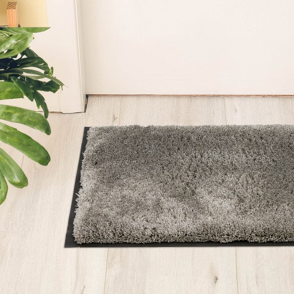 Grauer Shaggy-Teppich vor einer Tür auf einem hellen Holzboden.