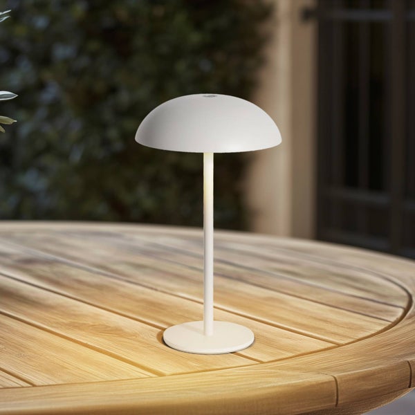 Tragbare weiße Tischleuchte in Pilzform auf einem hölzernen Gartentisch mit warmem Lichtschein.