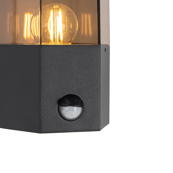 Moderne Außenwandleuchte mit Bewegungsmelder, schwarzem Metallgehäuse und klarem Glasschirm mit leuchtendem LED-Leuchtmittel.