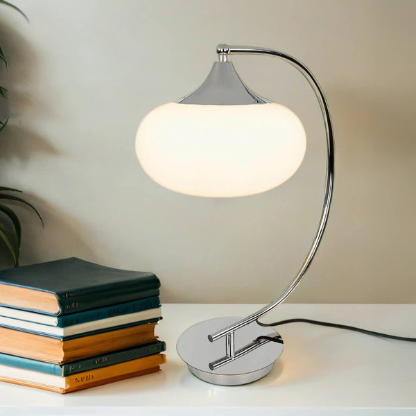 Tischleuchte mit Schirm und verchromtem Gestell neben einem Bücherstapel