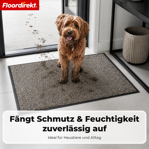 Floordirekt Logo. Brauner Hund auf einer grau melierten Schmutzfangmatte im Eingangsbereich mit schlammigen Pfotenabdrücken.