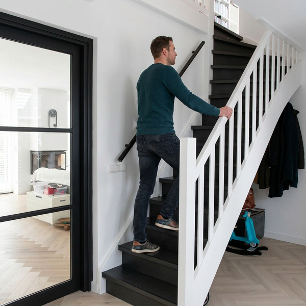 Moderne Treppe mit dunklen Stufen und weißem Holzgeländer. Ein Mann steigt die Treppe in einem hellen, organisierten Flur hinauf.