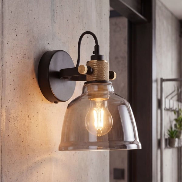 Wandleuchte im Industrie-Stil mit klarem Glasschirm und Messing-Details an einer grauen Wand montiert.