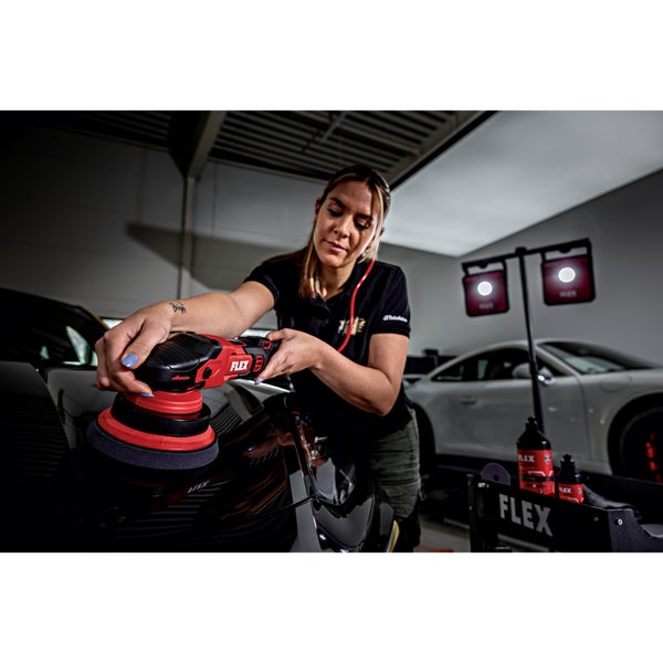 Eine Person poliert die Motorhaube eines schwarzen Autos mit einer elektrischen Poliermaschine von FLEX in einer professionellen Werkstatt.