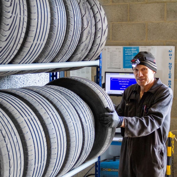 Reifenregal mit Autoreifen und Mechaniker in einer Werkstatt