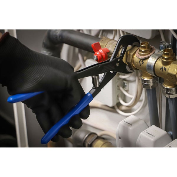 Eine Person mit Handschuhen verwendet eine Zange an einem Heizungsventil.