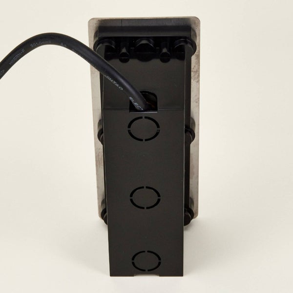 Rückansicht eines schwarzen Elektrogehäuses mit Stromkabel, Montageplatte aus Metall und Kabeldurchführungen.