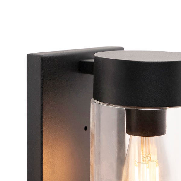 Nahaufnahme einer schwarzen Außenwandleuchte mit zylindrischem Klarglas und leuchtendem Filament-Leuchtmittel.