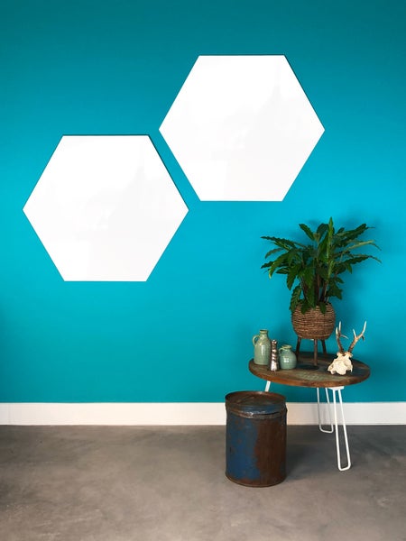 Zwei weiße hexagonale Whiteboards an einer Wand über einem runden Holztisch mit einer Zimmerpflanze und Dekoration.