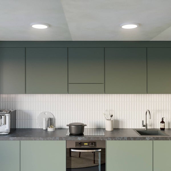 Moderne Küche mit grünen Schränken, weißem Fliesenspiegel und runden LED-Deckenleuchten für helle, gleichmäßige Beleuchtung.