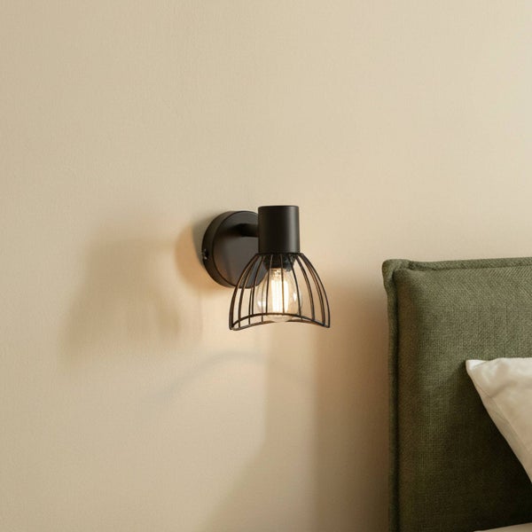 Schwarze Wandleuchte mit Käfigschirm neben einem Bett