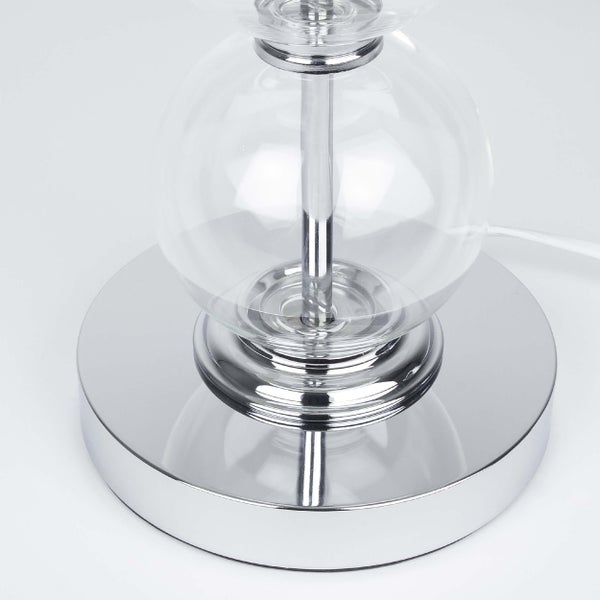 Detailansicht einer Tischleuchte mit transparentem Glasschirm und verchromtem Fuß