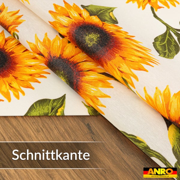 Wachstuch-Tischdecke mit Sonnenblumen-Motiv, Detailansicht der Schnittkante auf einer Holzoberfläche. ANRO Logo.