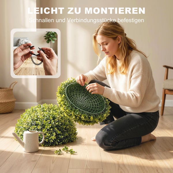 Eine Frau montiert eine künstliche Buchsbaumkugel aus zwei Hälften durch Zusammenstecken der Verbindungsstücke in einem hellen, organisierten Raum.