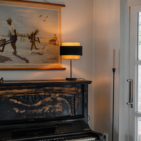 Tischlampe mit dreiteiligem Schirm auf einem antiken Klavier in einem Raum mit warmer Beleuchtung.