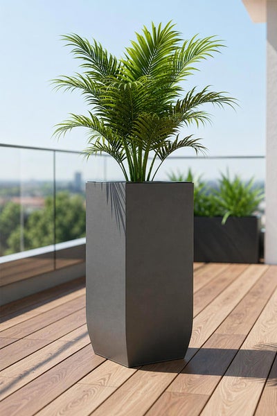 Hohes, quadratisches Pflanzgefäß in Dunkelgrau mit grüner Palme auf einer Holzterrasse mit Glasgeländer.