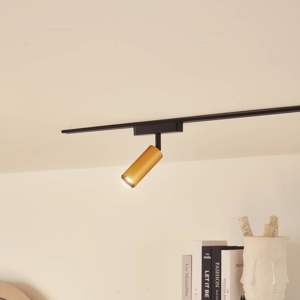 Goldfarbener Strahler für ein Schienensystem, montiert an einer schwarzen Deckenleiste.