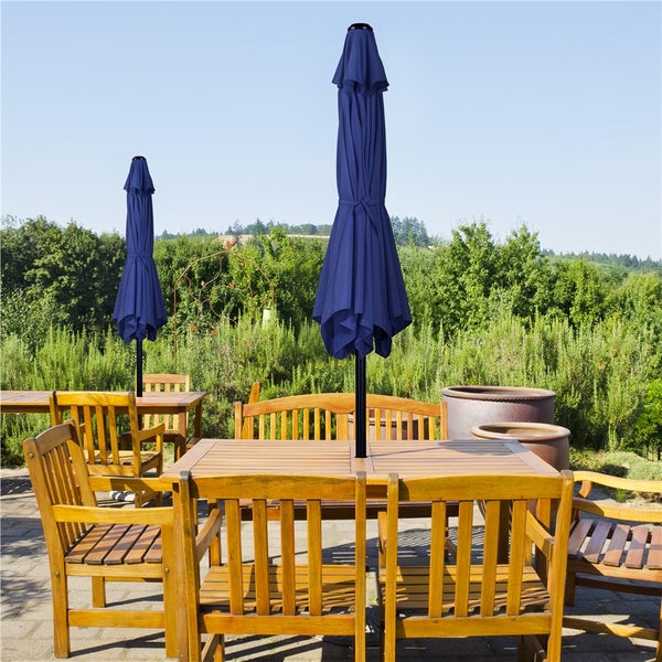 Szene im Freien mit mehreren Gartensitzgruppen aus Holz und zugehörigen, geschlossenen Sonnenschirmen.