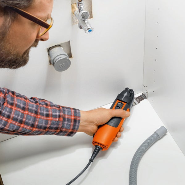 Oszillierendes Multifunktionswerkzeug mit Hartmetall-Segmentsägeblatt beim Ausfräsen von Fliesenfugen auf einem Boden aus grauen Fliesen.