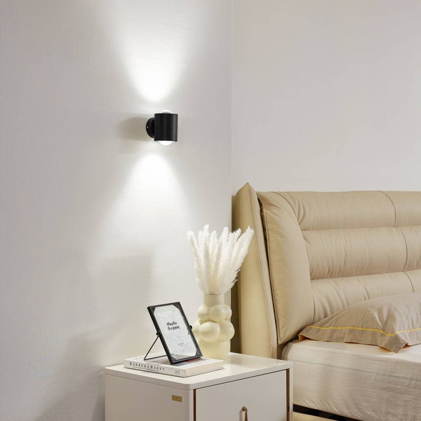 Szene mit einer schwarzen Wandleuchte, einem Nachttisch, einer Vase und einem Bett