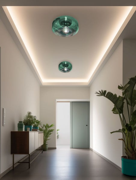 Zwei moderne Deckenleuchten aus grünem Glas in einem hellen, minimalistischen Flur mit indirekter Deckenbeleuchtung und Zimmerpflanzen.
