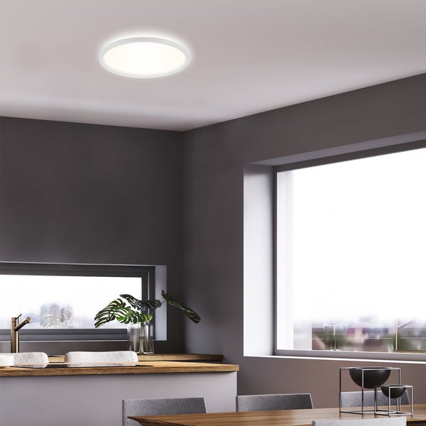 Flache runde LED-Deckenleuchte in einer modern gestalteten hellen Küche mit großen Fenstern und grauen Wänden.