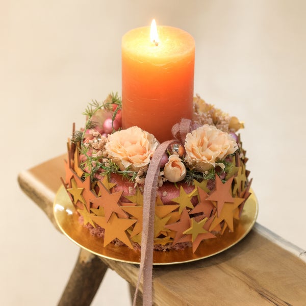Adventskranz mit Kerze, Blumen und Sternen auf einem Holzhocker