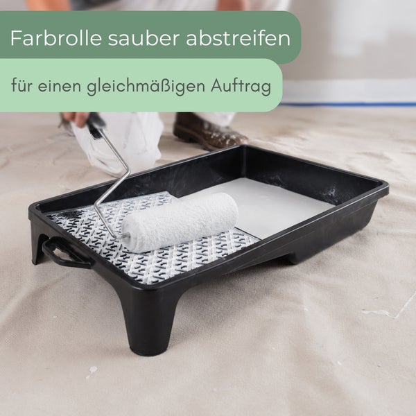 Eine Farbrolle wird in einer Farbwanne am Abstreifgitter für einen gleichmäßigen Farbauftrag abgestrichen.