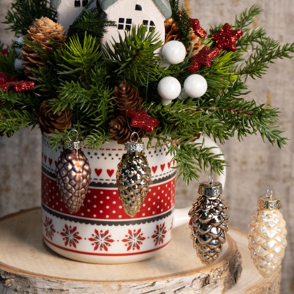 Dekorative Tasse mit Tannenzweigen, Zapfen und Christbaumschmuck in Zapfenform