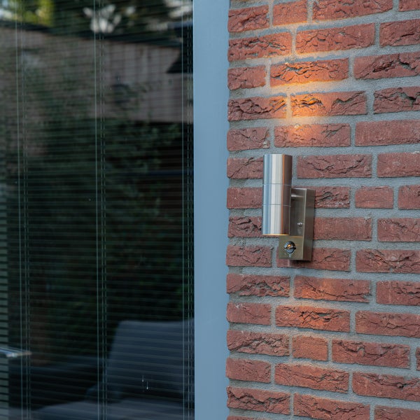 Moderne Außenwandleuchte aus Edelstahl mit Bewegungsmelder, montiert an einer Ziegelwand, Up-and-Down-Lichteffekt.