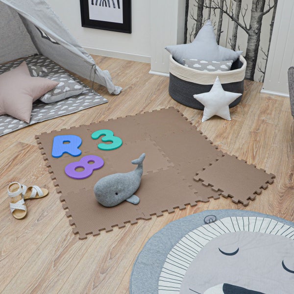 Helle Kinderzimmer-Szene mit einer braunen Schaumstoff-Puzzlematte auf Holzboden, einem Spielzelt, Kissen und Spielzeug.