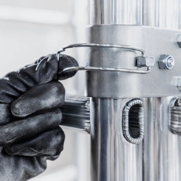 Hand mit Arbeitshandschuh an einem Metallgerüst befestigt